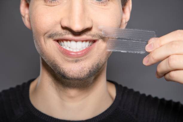 man with whitening strips next to his face 